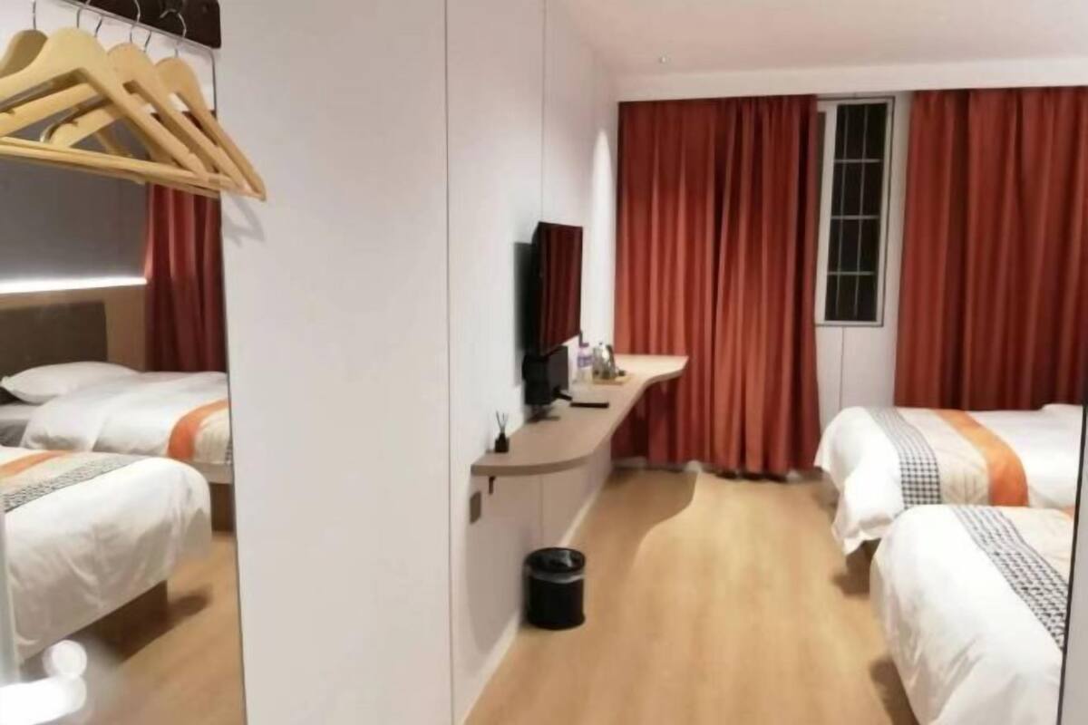 A hotel room with two beds, a desk, a TV, and a window with curtains.