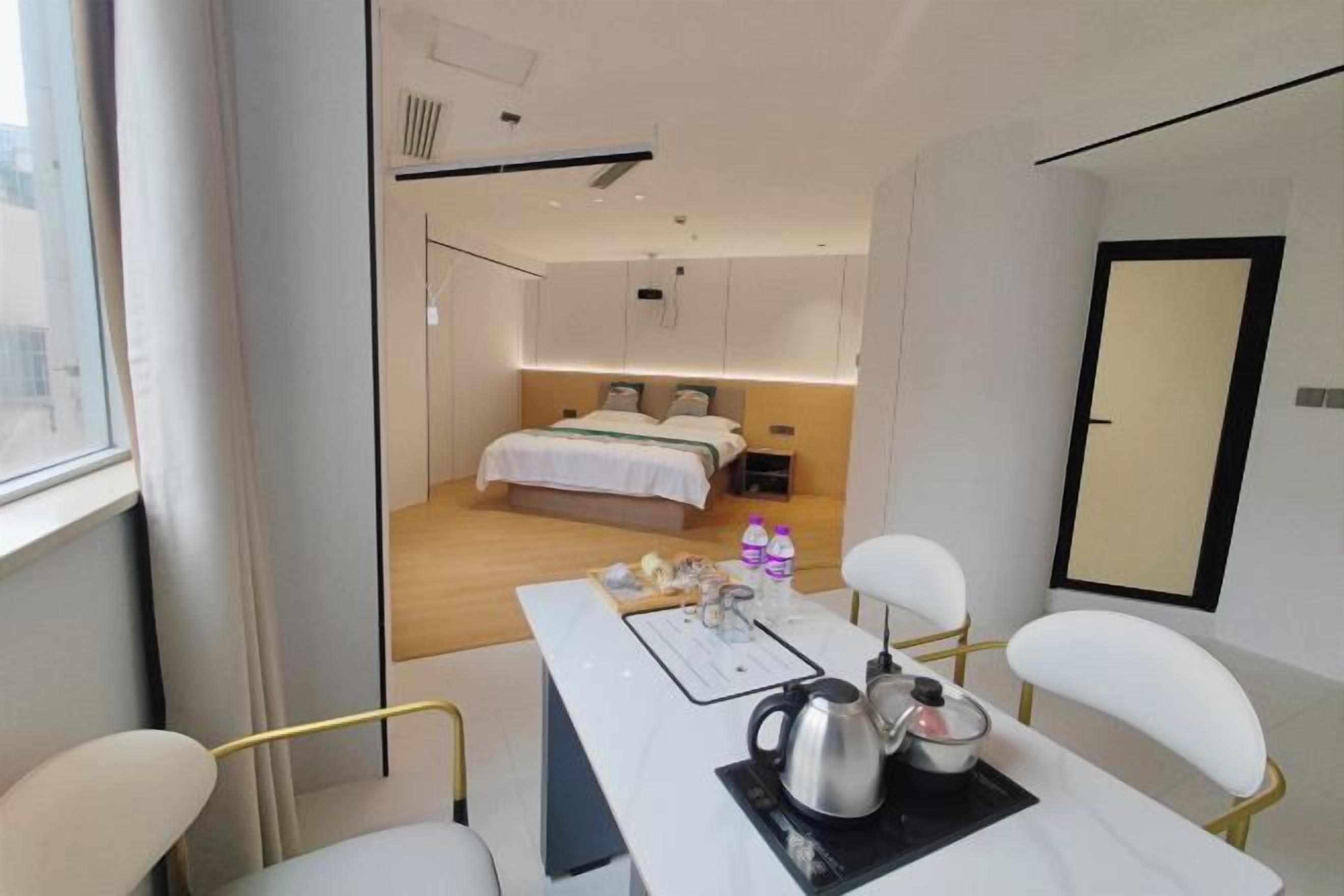 Una habitación de hotel moderna con una cama, una mesa de comedor con sillas, un hervidor y una pequeña mesa con botellas.