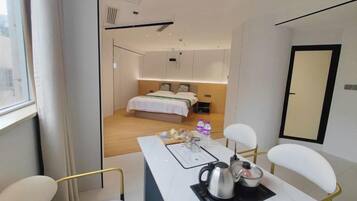 Una habitación de hotel moderna con una cama, una mesa de comedor con sillas, un hervidor y una pequeña mesa con botellas.