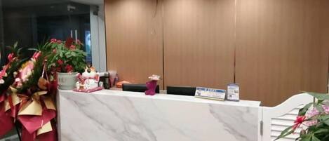 A reception desk with a marble top, wooden paneling on the wall, and a potted plant to the left.