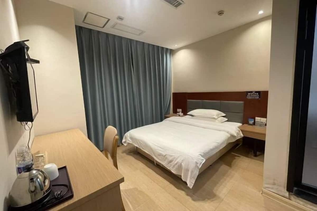 A hotel room with a bed, a desk, a chair, a television, and a curtain.