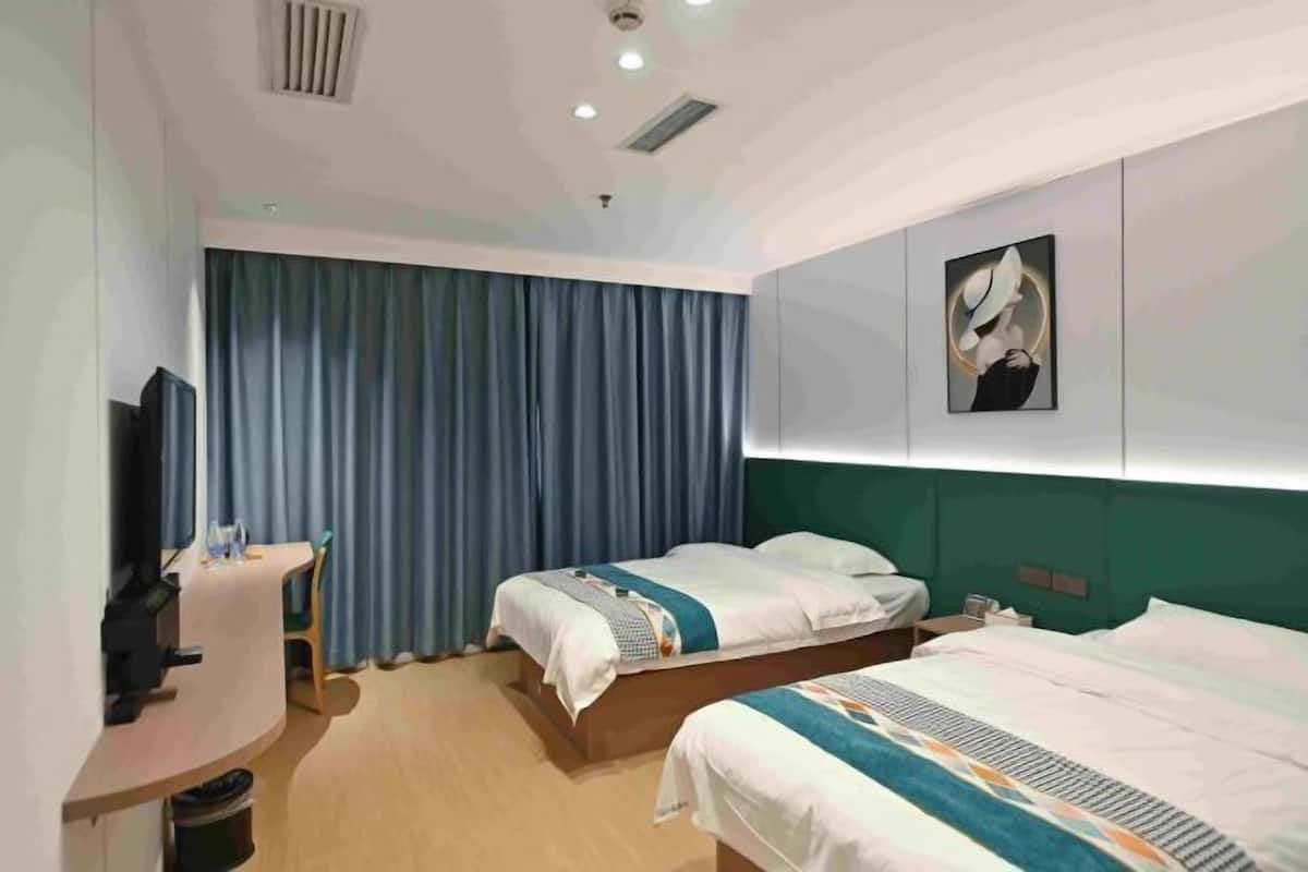 A hotel room with two beds, a desk, a television, and a large window with curtains.