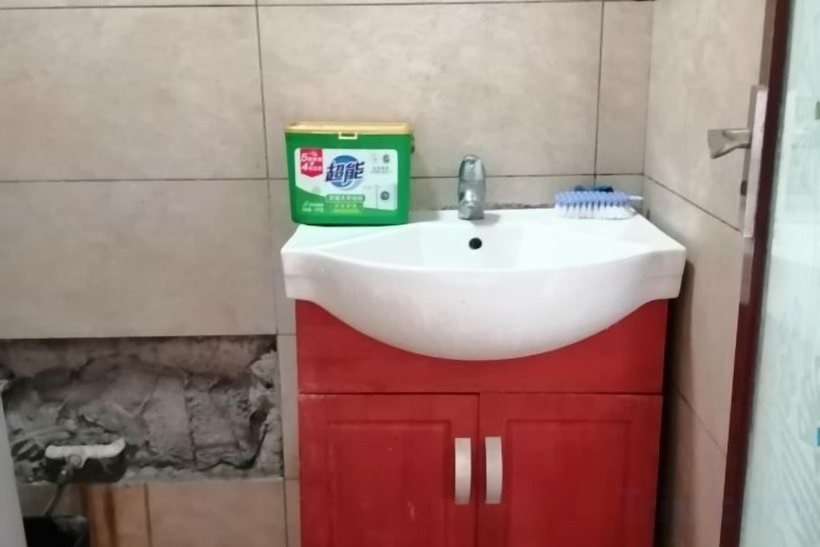 Un baño con un lavamanos blanco, un mueble rojo y una caja verde de detergente.