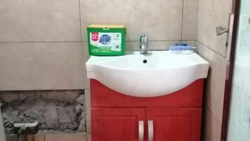 Un baño con un lavamanos blanco, un mueble rojo y una caja verde de detergente.