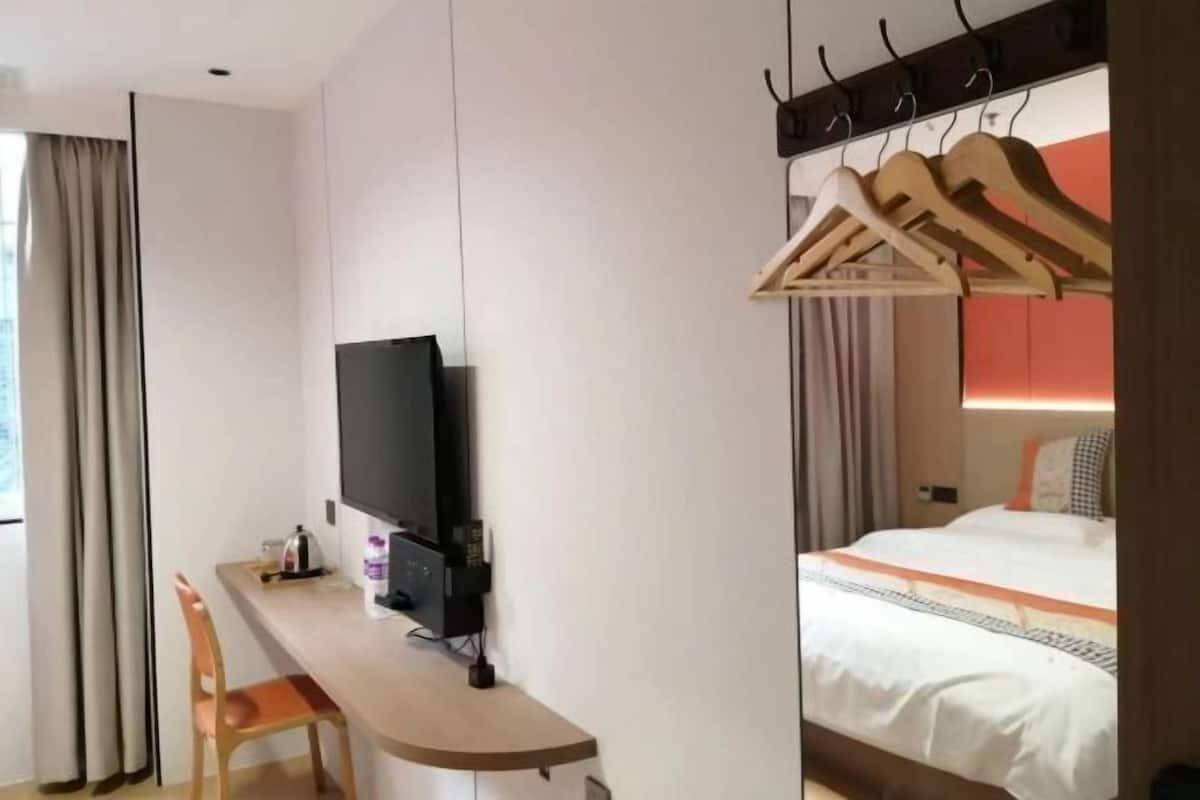 A hotel room with a bed, a desk with a chair, a television, and a coat rack.
