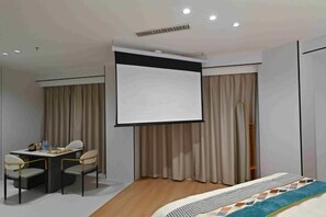 A hotel room with a bed, a desk with chairs, a projector screen, and curtains. - Sihe Haichuan Hostel (Nanping)