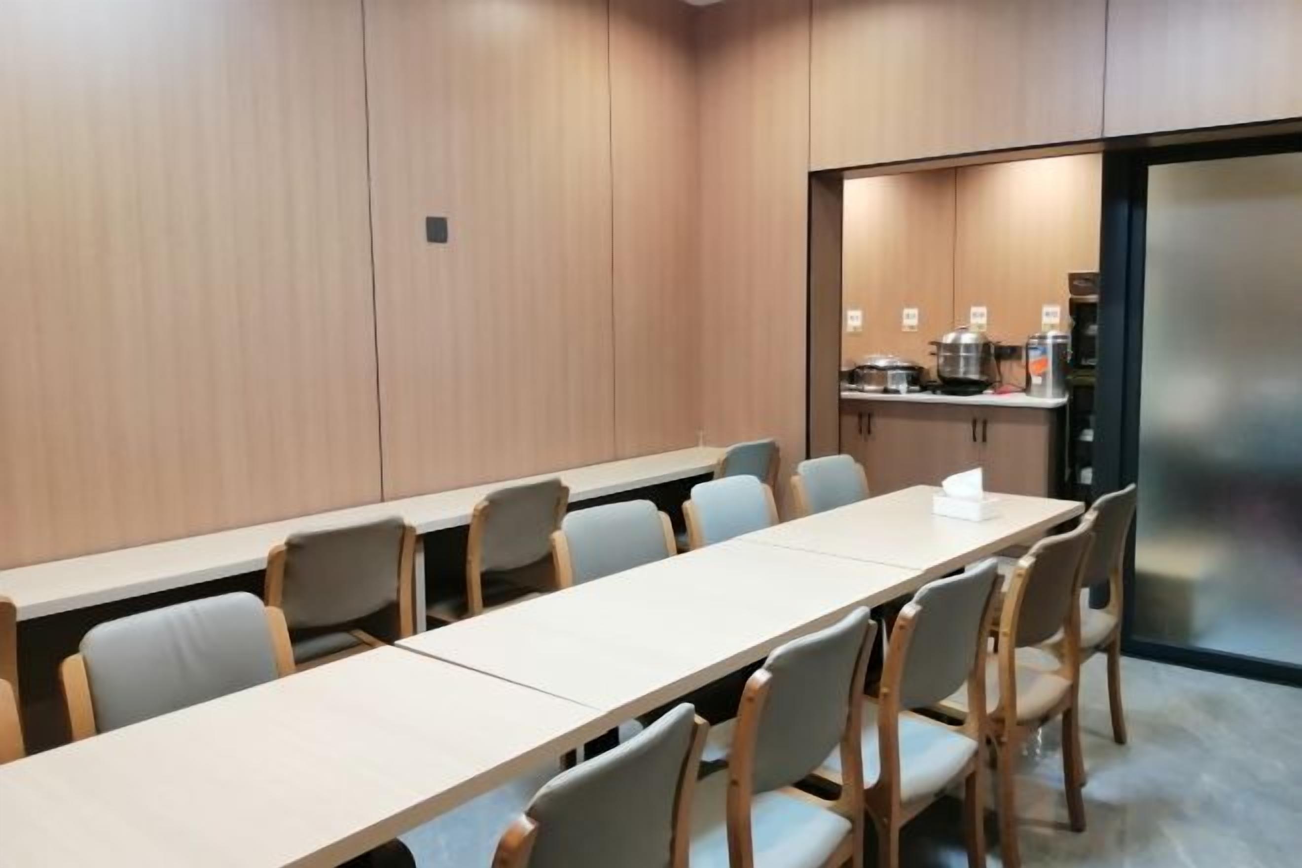 Una sala de conferencias con una larga mesa y sillas, una zona de kitchenette y una puerta de cristal que da a una cocina.