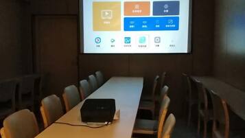 Un salón de conferencias con una mesa larga, sillas, un proyector y una pantalla mostrando una presentación.