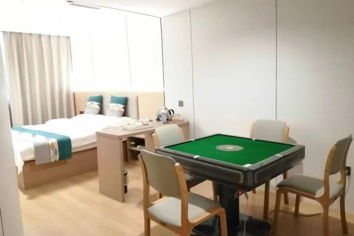 A hotel room with a bed, a desk, a pool table, and a window with curtains.