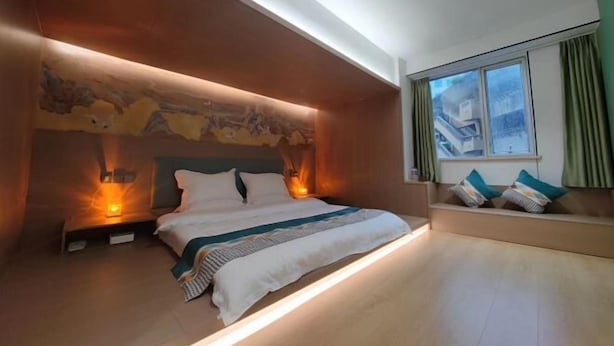 A modern bedroom with a bed, bedside lamps, a window with curtains, and a wall with a textured design. - Sihe Haichuan Hostel (Nanping)