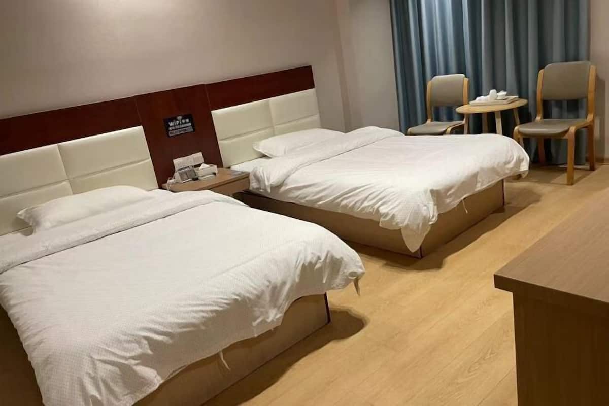 A hotel room with two beds, a wooden headboard, a small table with chairs, and a sign indicating Wi-Fi availability.