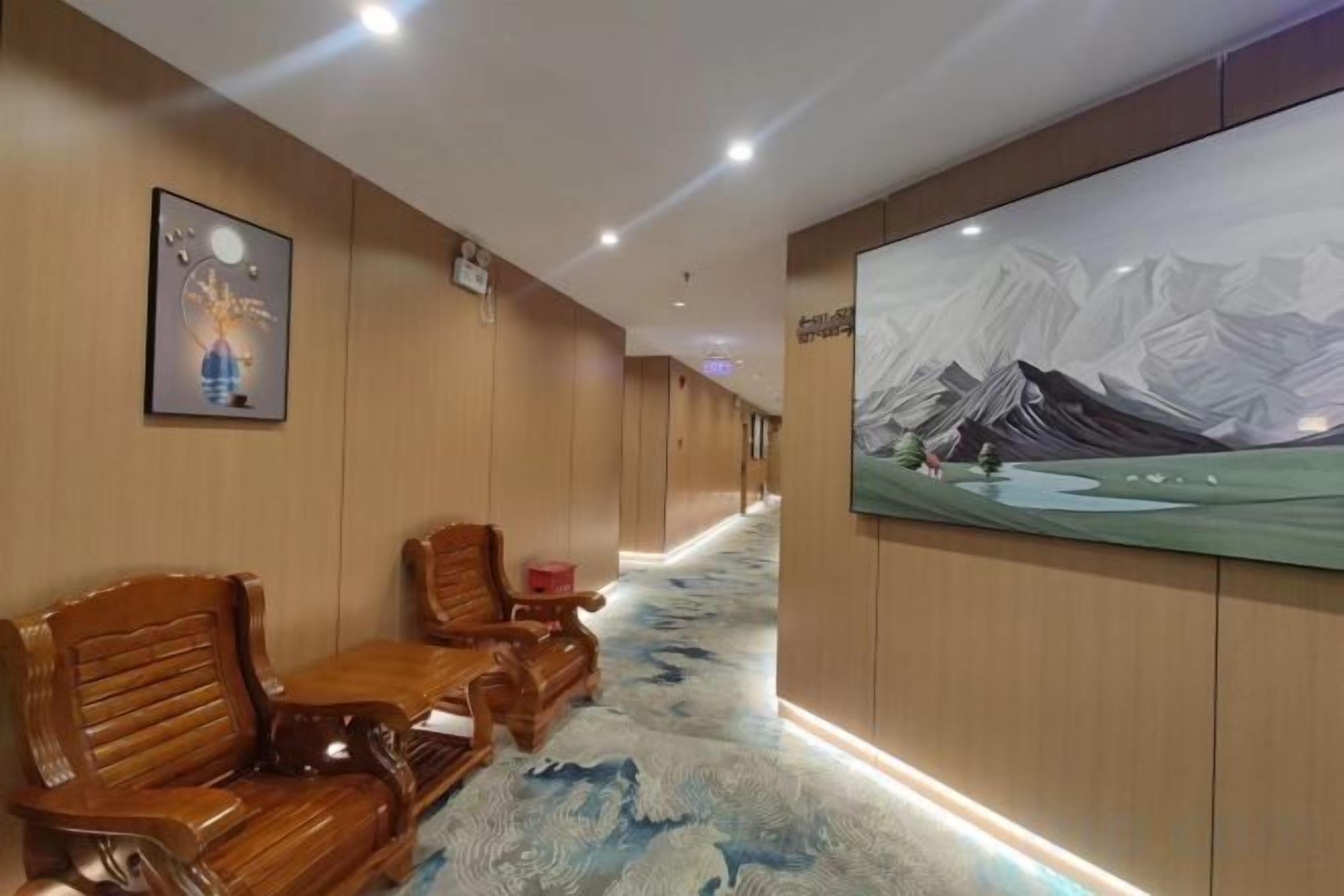 A hotel corridor with wooden chairs, a carpeted floor, and a large wall painting.