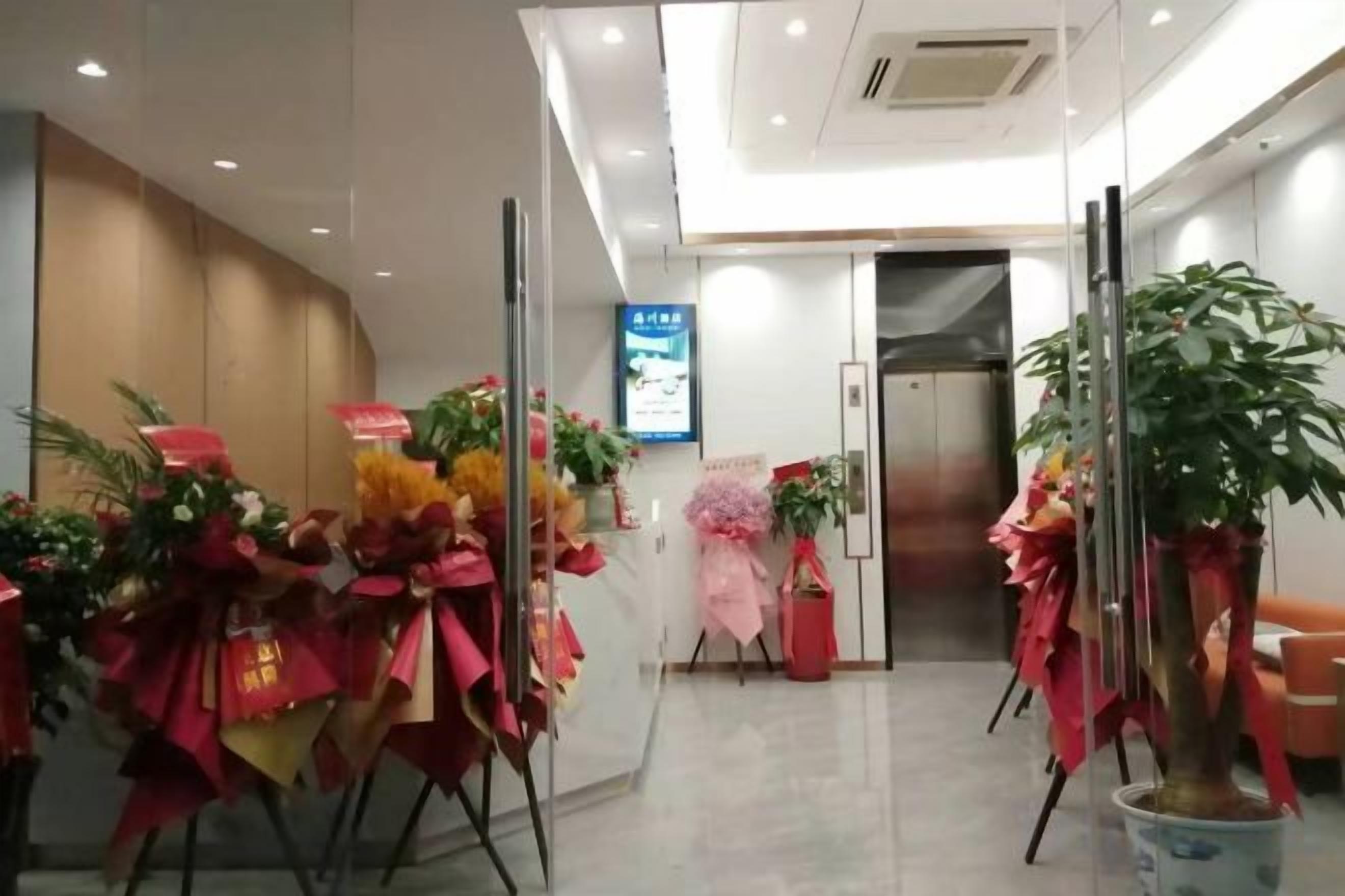 A hotel lobby with a reception desk, potted plants, and a digital screen.