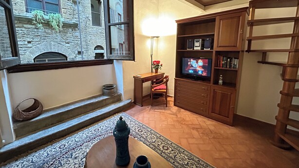 Un salon chaleureux avec un mur en pierre, un escalier en bois, un téléviseur et un coin repas.