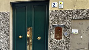 Une porte à deux battants, peinte en vert, avec une poignée en laiton, une plaque portant le numéro « 2 » et une caméra de surveillance au-dessus.