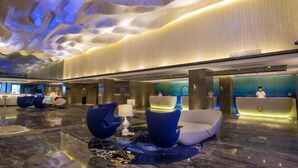 Un moderno vestíbulo de hotel con piso de mármol, asientos azules y blancos, una recepción y un diseño de techo único.