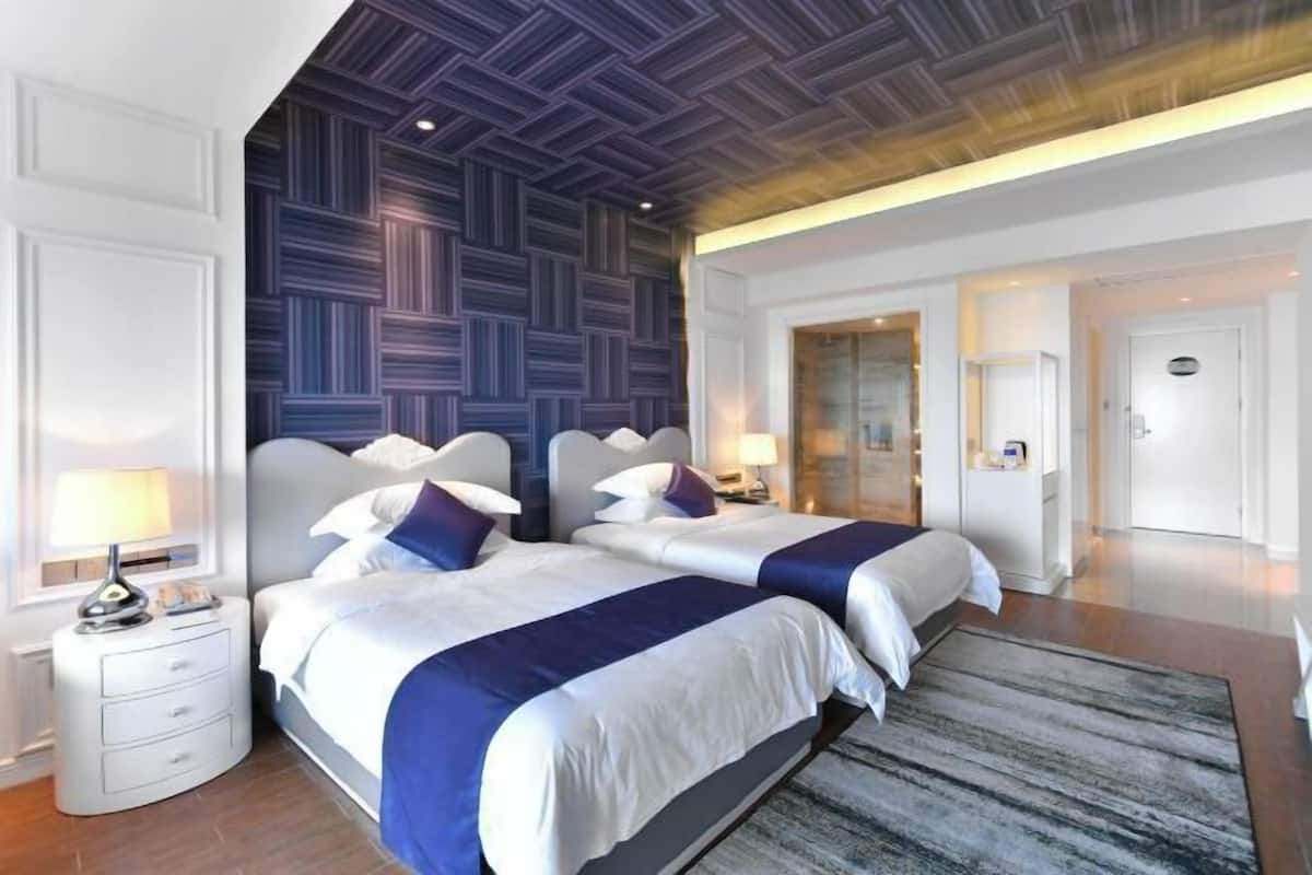 Ein modernes Hotelzimmer mit zwei Betten, einem großen Fenster und einer Holzbalkendecke.