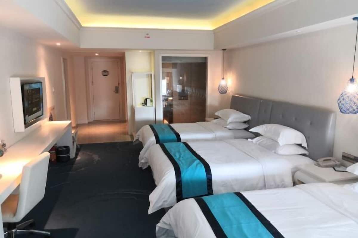 Ein Hotelzimmer mit drei Betten, einem Schreibtisch und einem Fernseher.