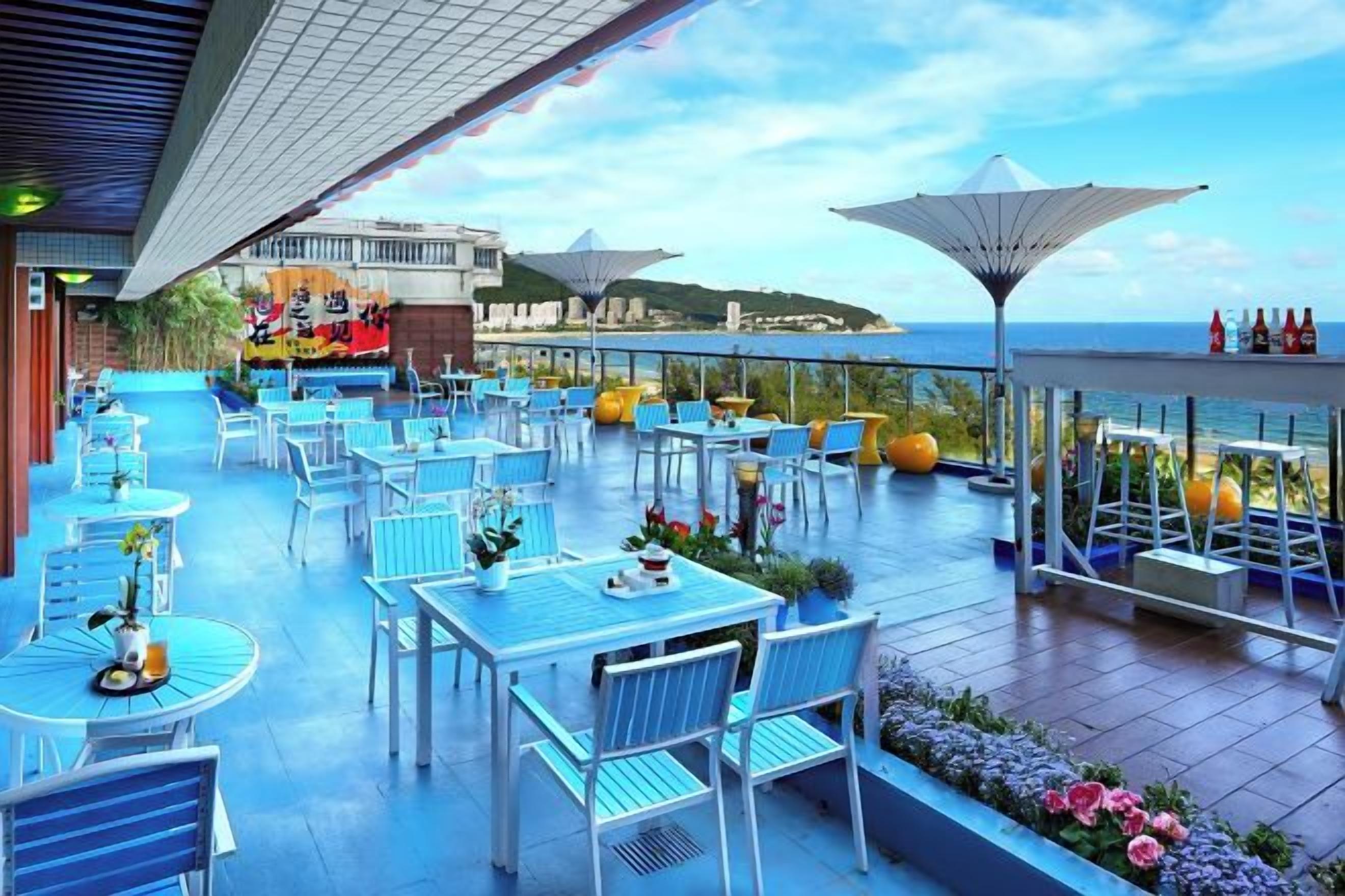 An outdoor terrace with tables and chairs, a view of the sea, and umbrellas.
