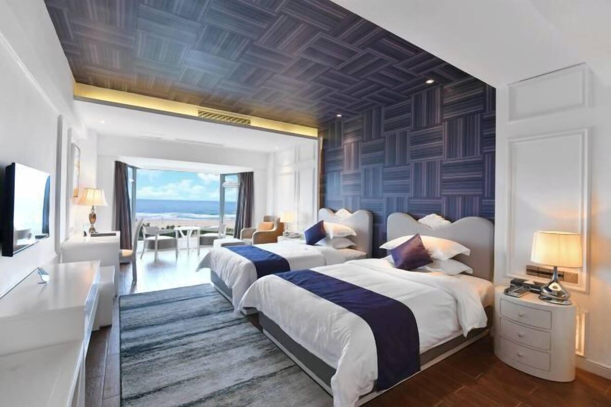 Ein modernes Hotelzimmer mit zwei Betten, einem großen Fenster mit Blick, einem Flachbildfernseher und einem Schreibtisch mit Lampe.