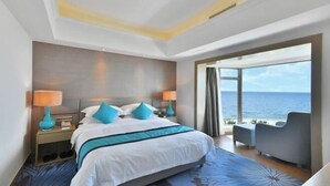 Una habitación de hotel moderna con una cama grande, dos lámparas de noche, vista al mar y un área de descanso con vistas.