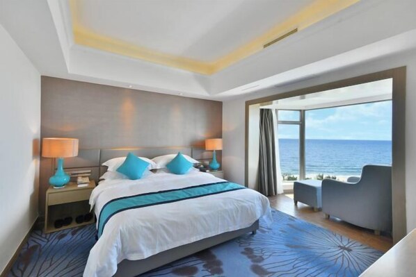 A modern hotel room with a large bed, two bedside lamps, a view of the sea, and a seating area with a view. - Ocean Rise Hotel (Yangjiang)