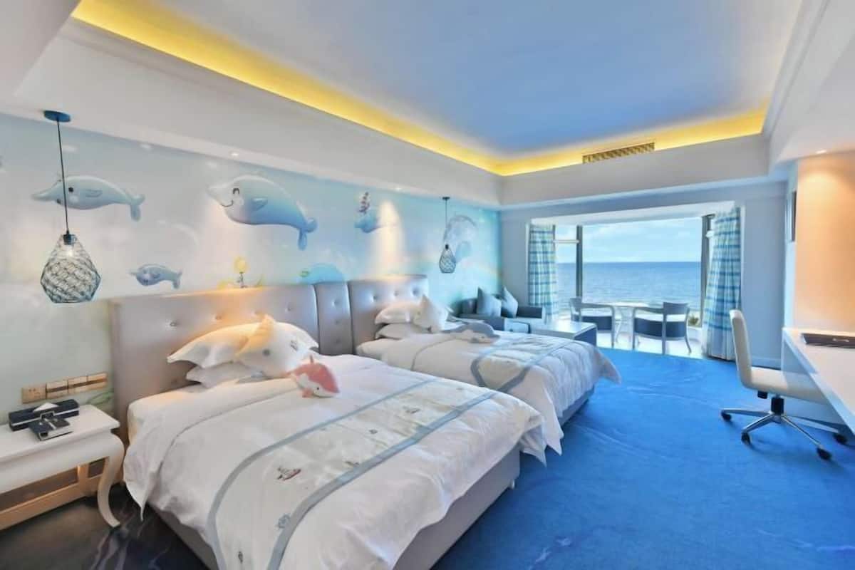 Ein Hotelzimmer mit zwei Betten, einem Schreibtisch und Meerblick.