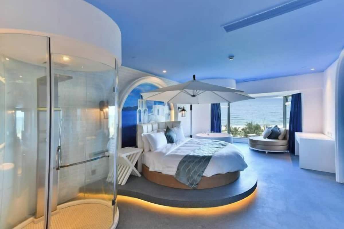 Ein modernes Schlafzimmer mit einem gewölbten Bett, einer Duschkabine aus Glas und Blick aufs Meer.