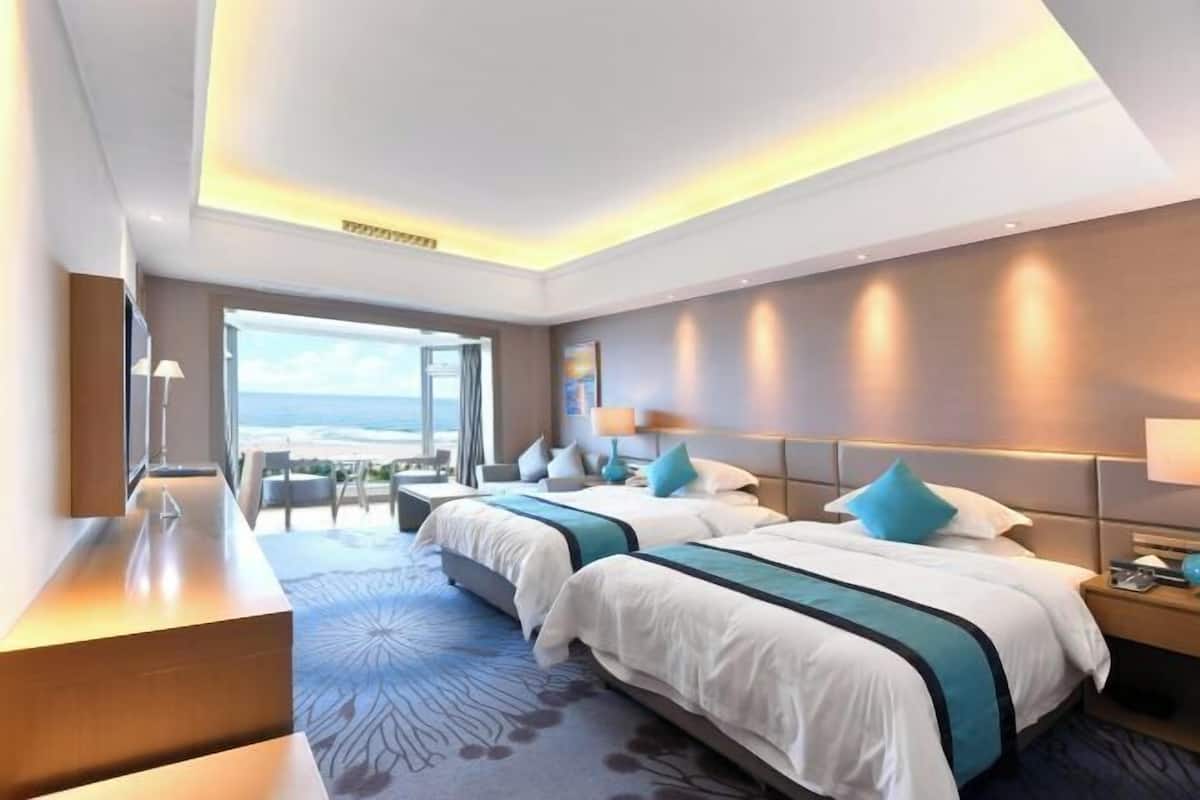 Ein modernes Hotelzimmer mit zwei Betten, einem Schreibtisch und Blick auf den Strand.