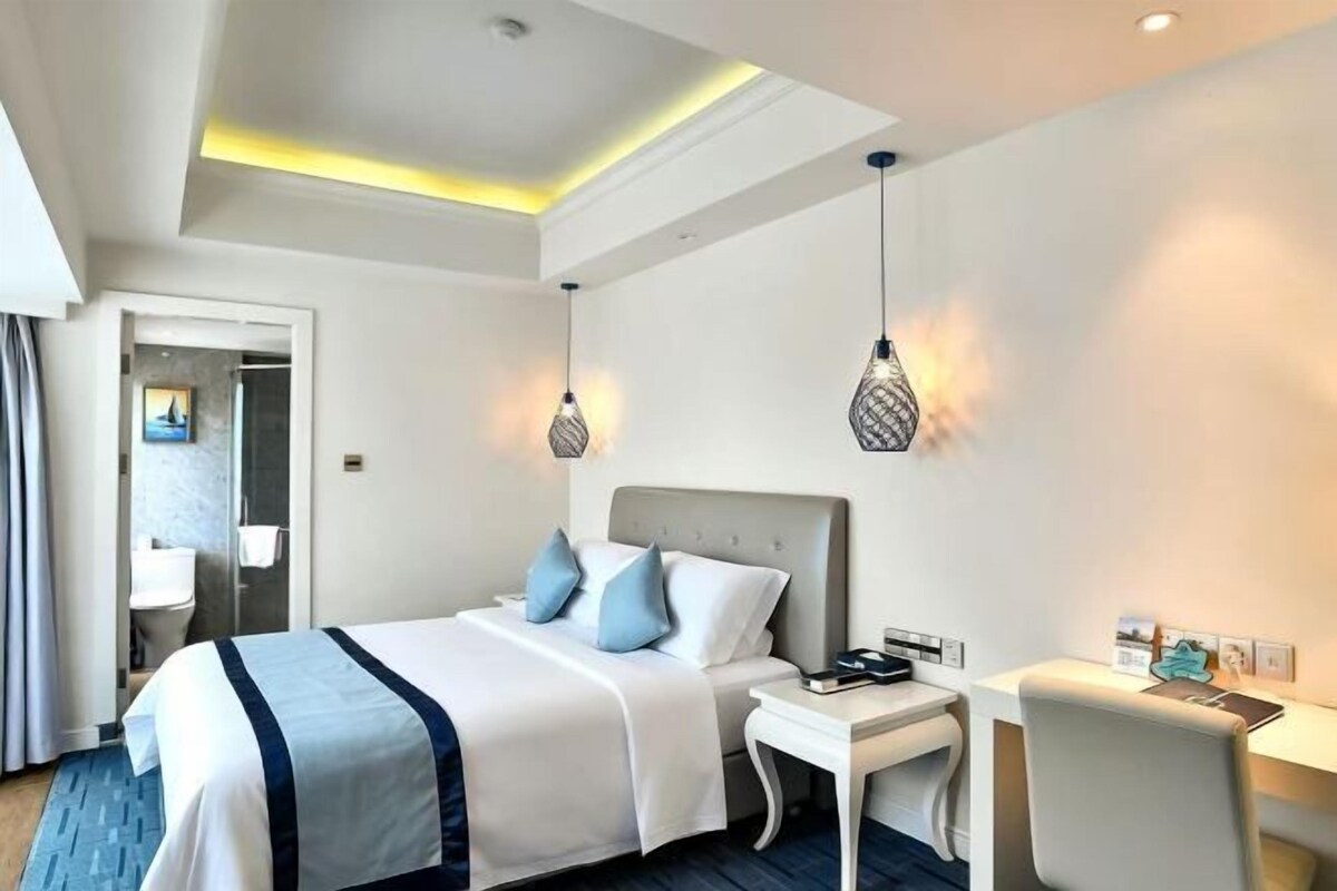 A hotel room with a bed, bedside table, desk, and hanging lamps.