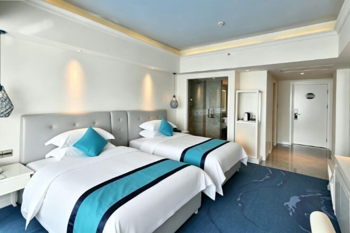 A hotel room with two beds, a desk, and a door leading to a bathroom.