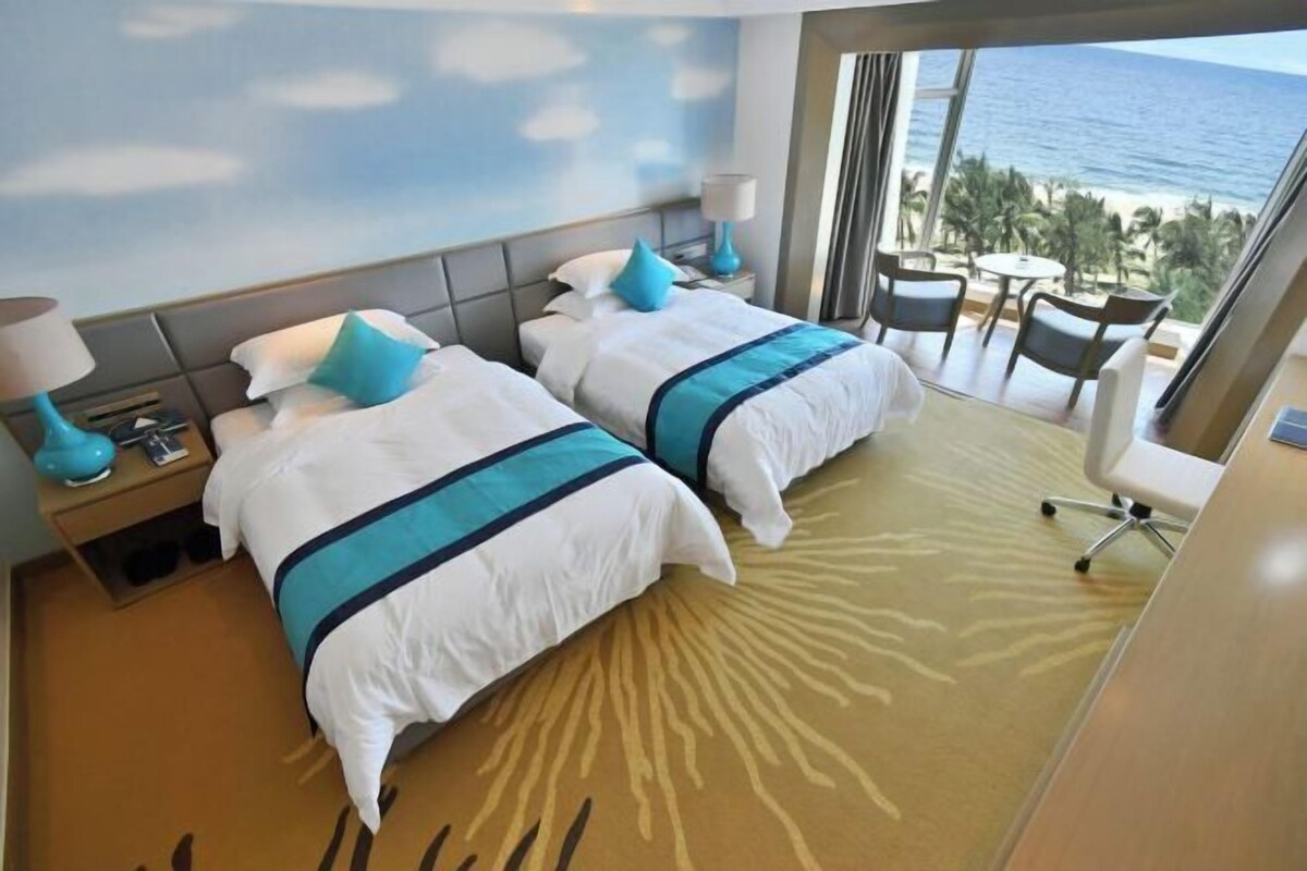 A hotel room with two beds, a view of the beach, and a balcony with a table and chairs.