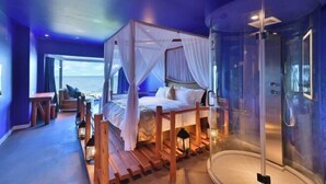 Un dormitorio con cama con dosel, ducha con cabina de cristal y vistas al mar.
