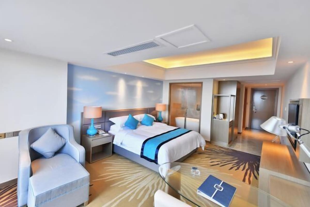 A hotel room with a bed, a chair, a desk, a lamp, and a glass table.