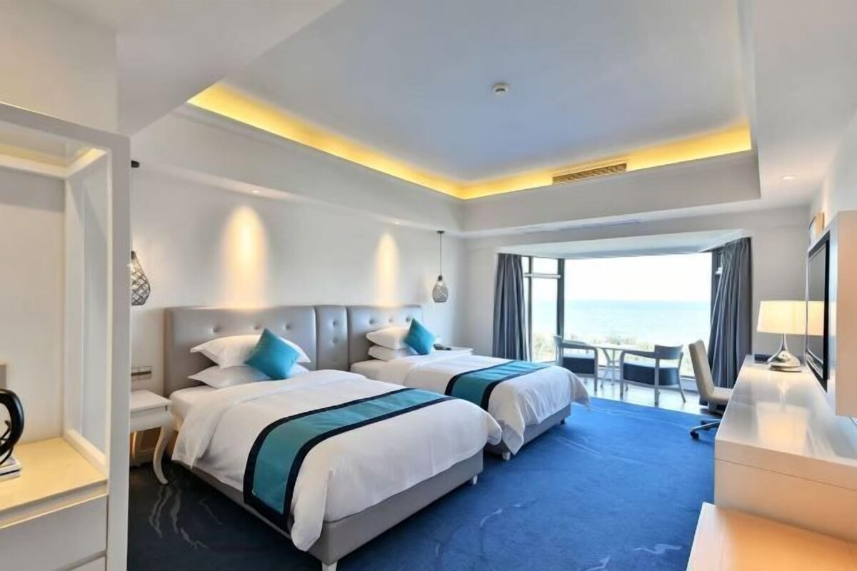 A hotel room with two beds, a desk, and a view of the ocean.