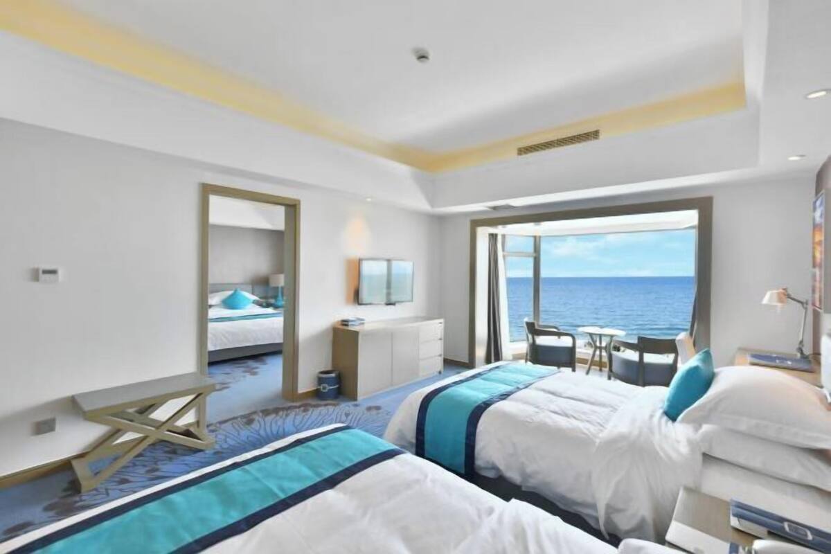 Ein Hotelzimmer mit zwei Betten, einem Schreibtisch, einem Stuhl, einem kleinen Tisch und Blick auf das Meer.