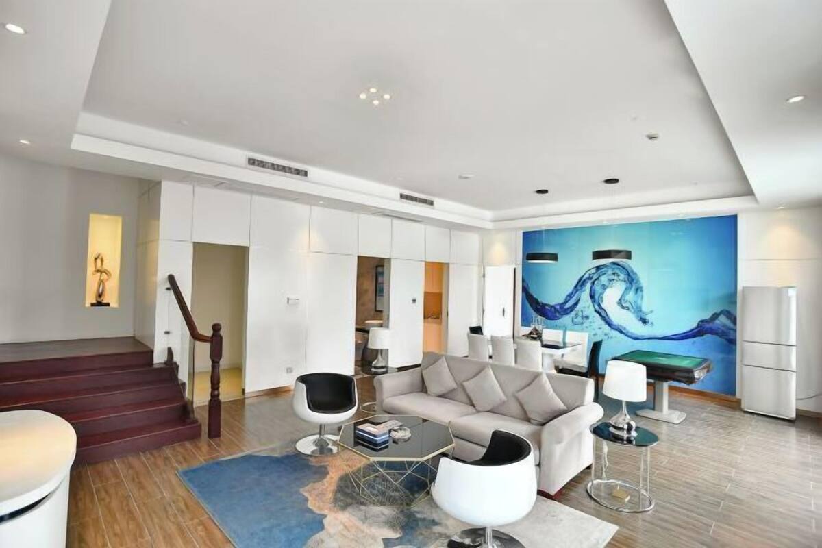Ein modernes Wohnzimmer mit Sofa, Couchtisch und Sesseln, einer Treppe und einem großen abstrakten Gemälde an der Wand.