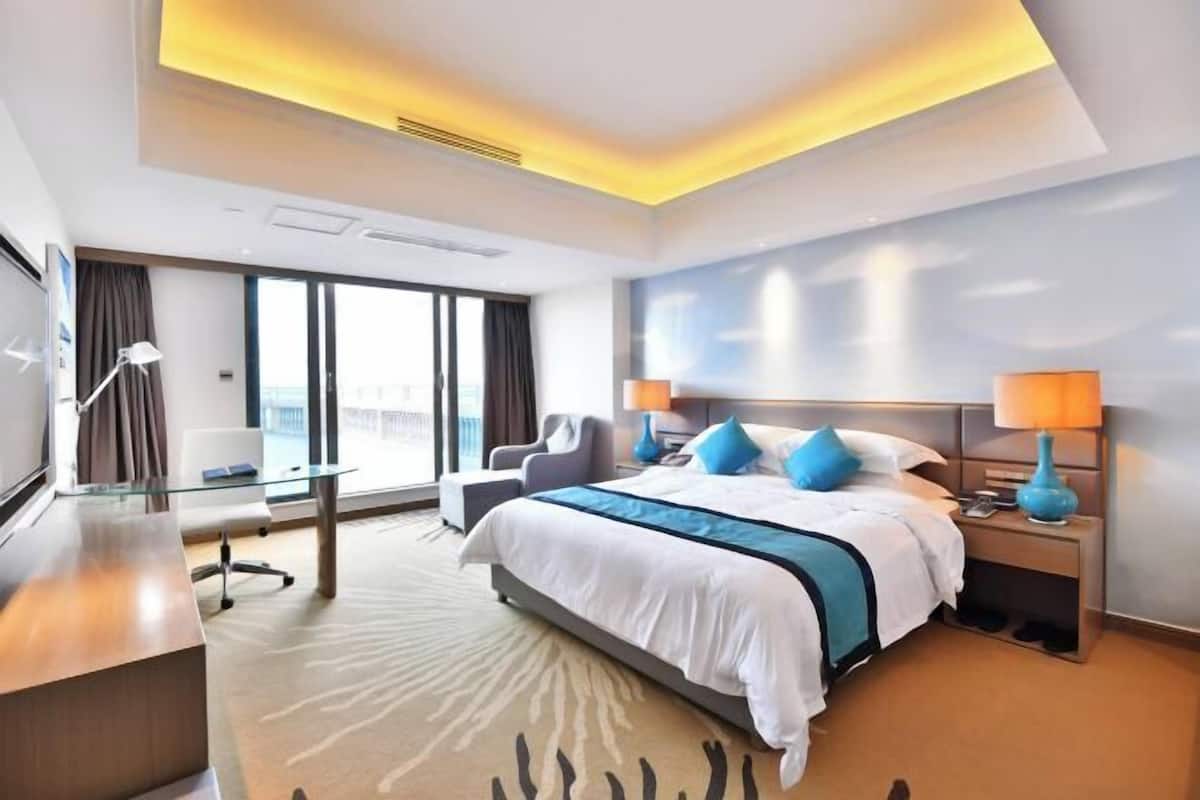 Ein modernes Hotelzimmer mit einem großen Bett, einem Schreibtisch, einem Sessel und Blick auf die Stadt.