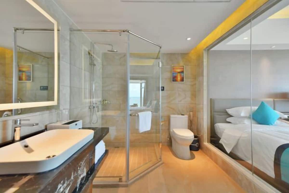 Ein modernes Hotelbad mit Duschkabine aus Glas, einem großen Spiegel, einem Waschbecken und einer Toilette.
