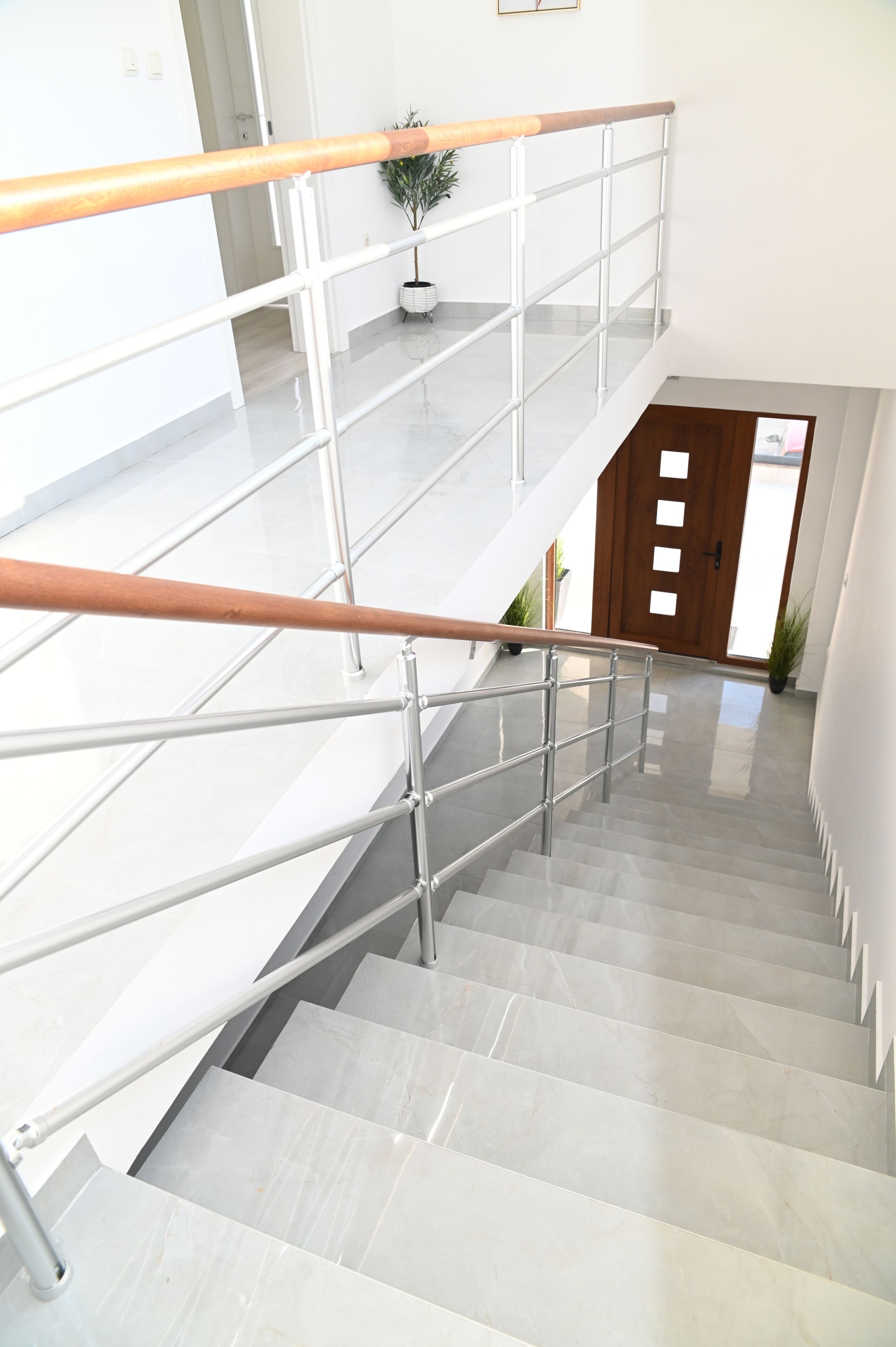 A modern staircase with metal railings and wooden handrails, leading to an upper floor.