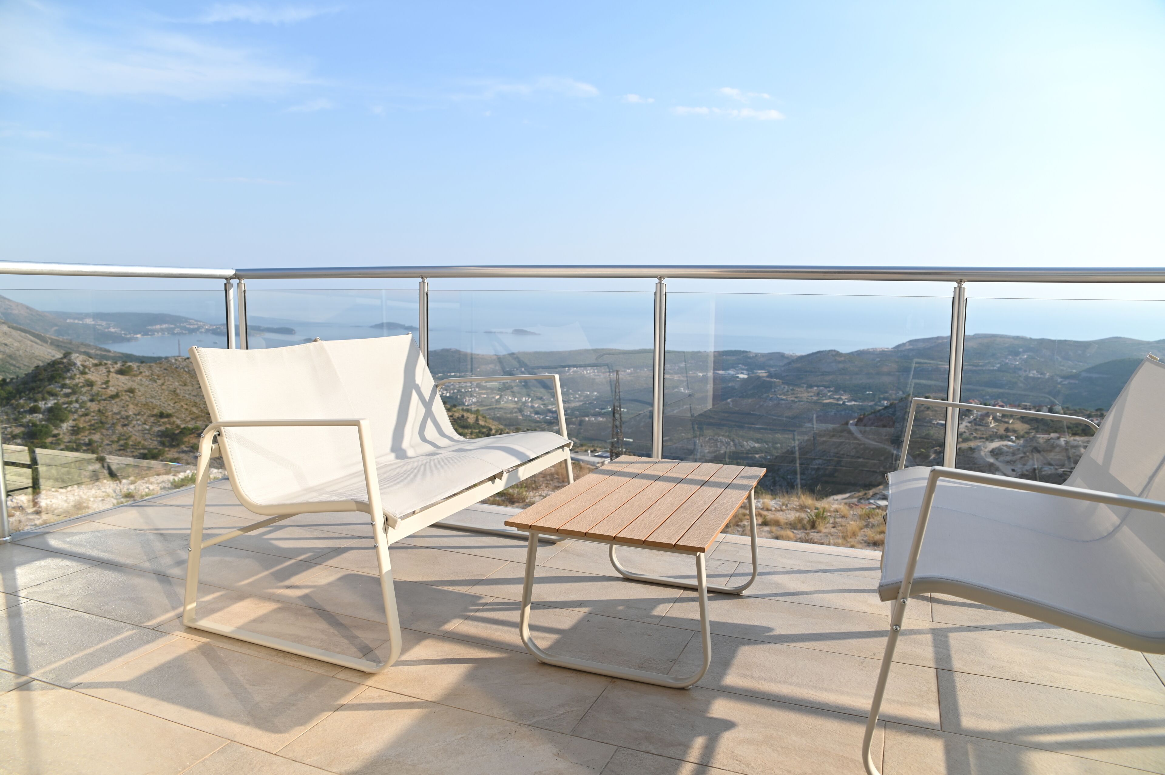 A balcony with two white chairs and a small table, overlooking a scenic landscape with hills and a body of water.