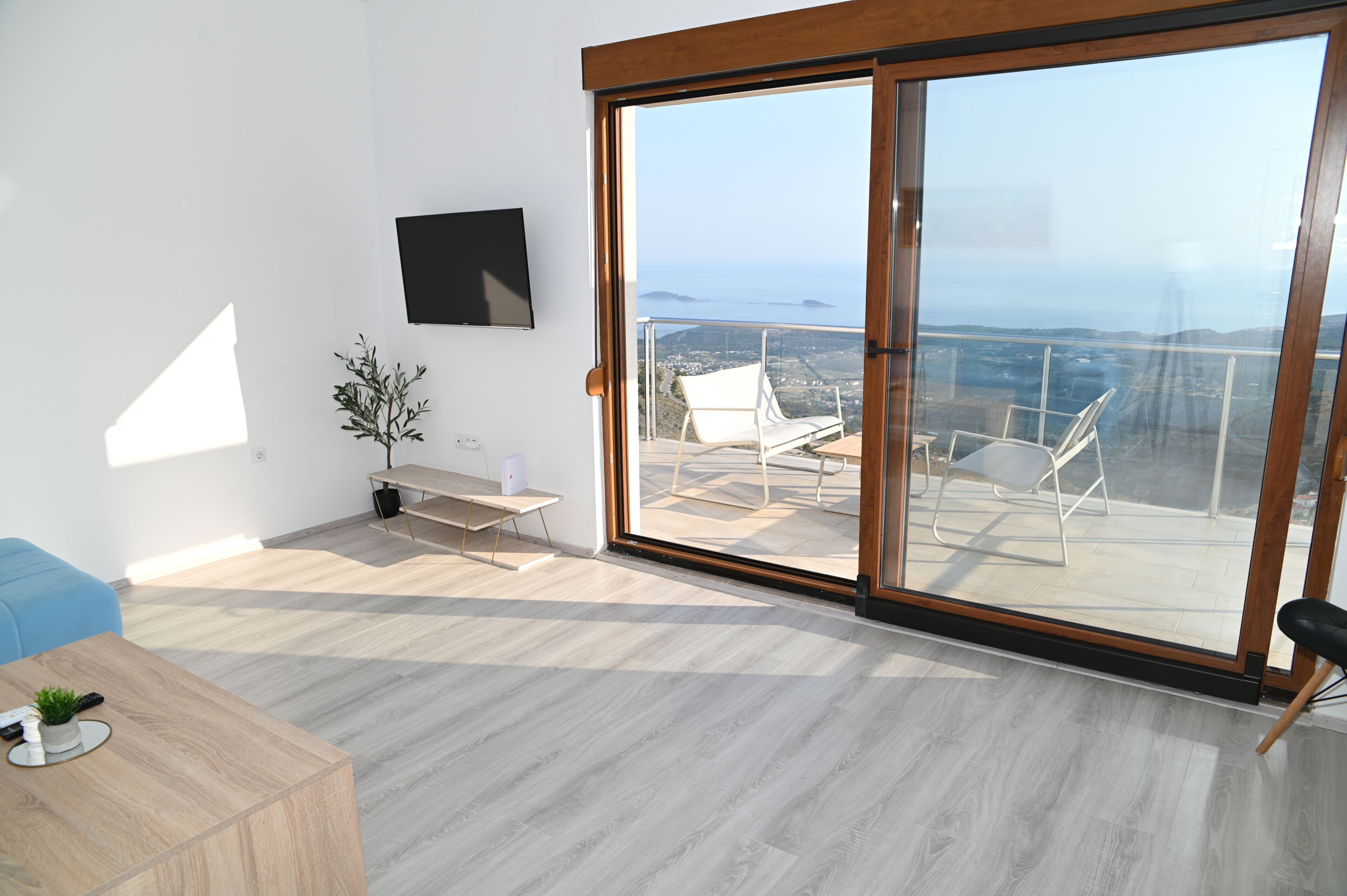 A modern living room with a large sliding glass door leading to a balcony with a view of the sea.