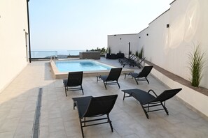 Área de piscina en la azotea con un jacuzzi, sillas de descanso y vistas al mar.