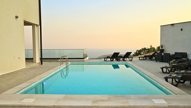 Une piscine rectangulaire à l’eau d’un bleu cristallin, entourée de chaises longues et bordée d’une balustrade en verre.