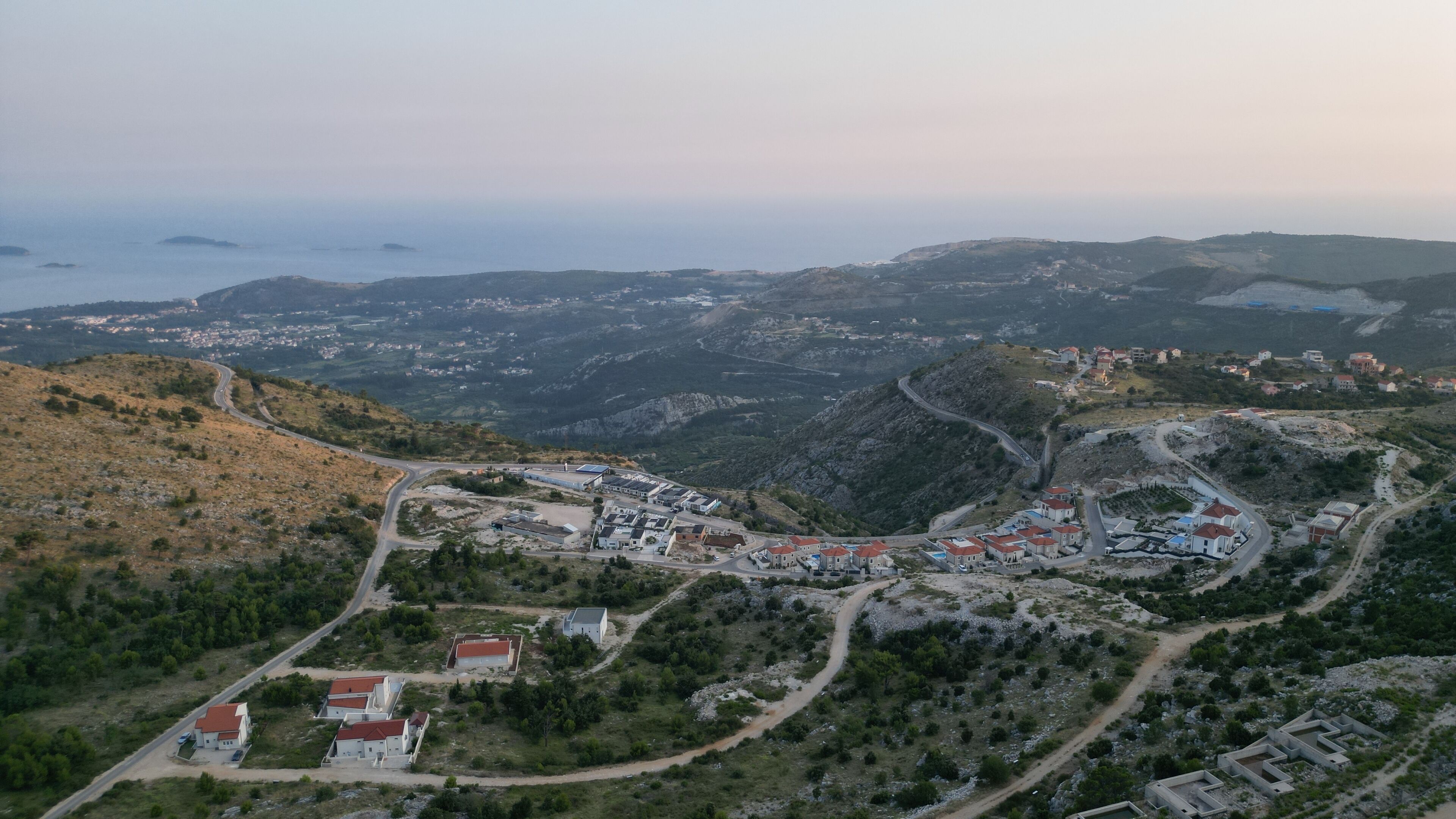 Vista aérea de un pueblo costero con carreteras sinuosas, edificios de tejados rojos y un paisaje montañoso.
