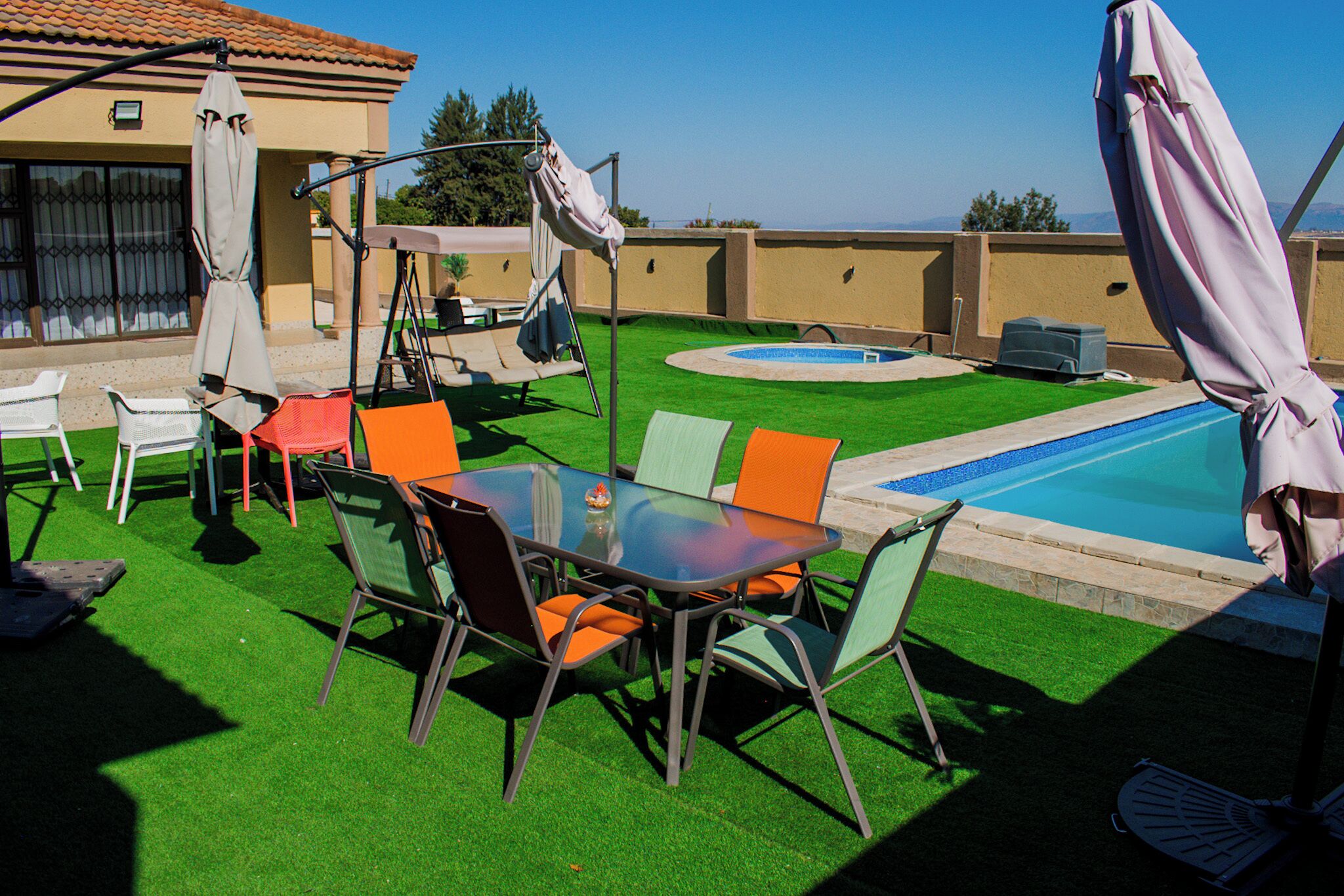 Un patio trasero con piscina, mobiliario exterior y un columpio.