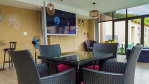Un comedor moderno con una mesa de vidrio y sillas de mimbre, un televisor de pantalla plana y vistas al exterior.