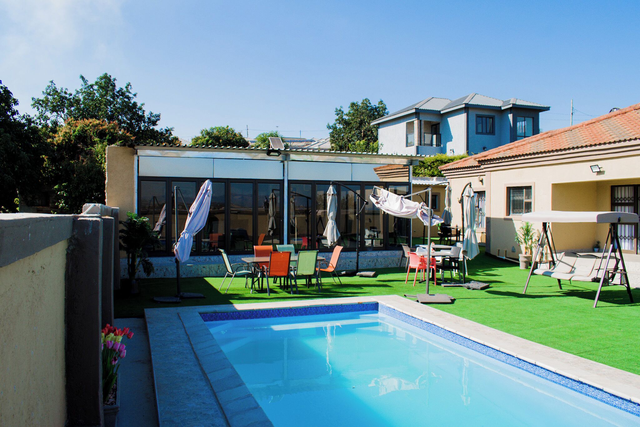 A swimming pool with a patio area, outdoor seating, and a building with large windows.