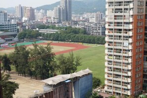 A high-rise building with multiple balconies, a sports field, and surrounding urban buildings. - Wings Hotel(East Railway Station Sports Institute Branch) (Guangzhou)