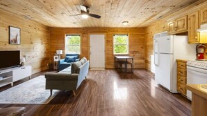 Interior de una cabaña con sala de estar, cocina y ventilador de techo.